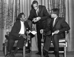 Bayard Rustin (seated at left) and Malcolm X (standing) at a debate in 1960